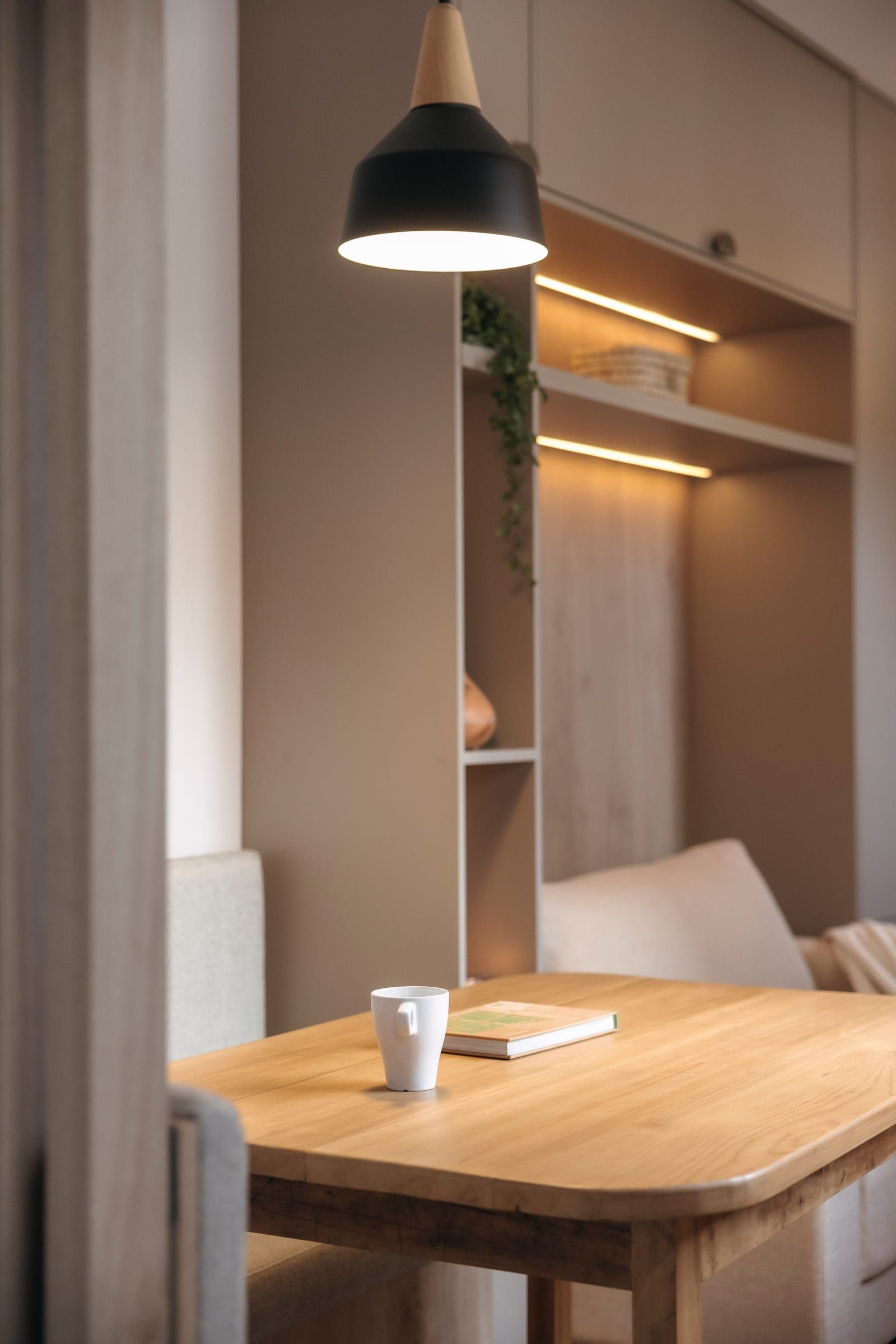Rincón con mesa de madera, banco tapizado y estantería iluminada