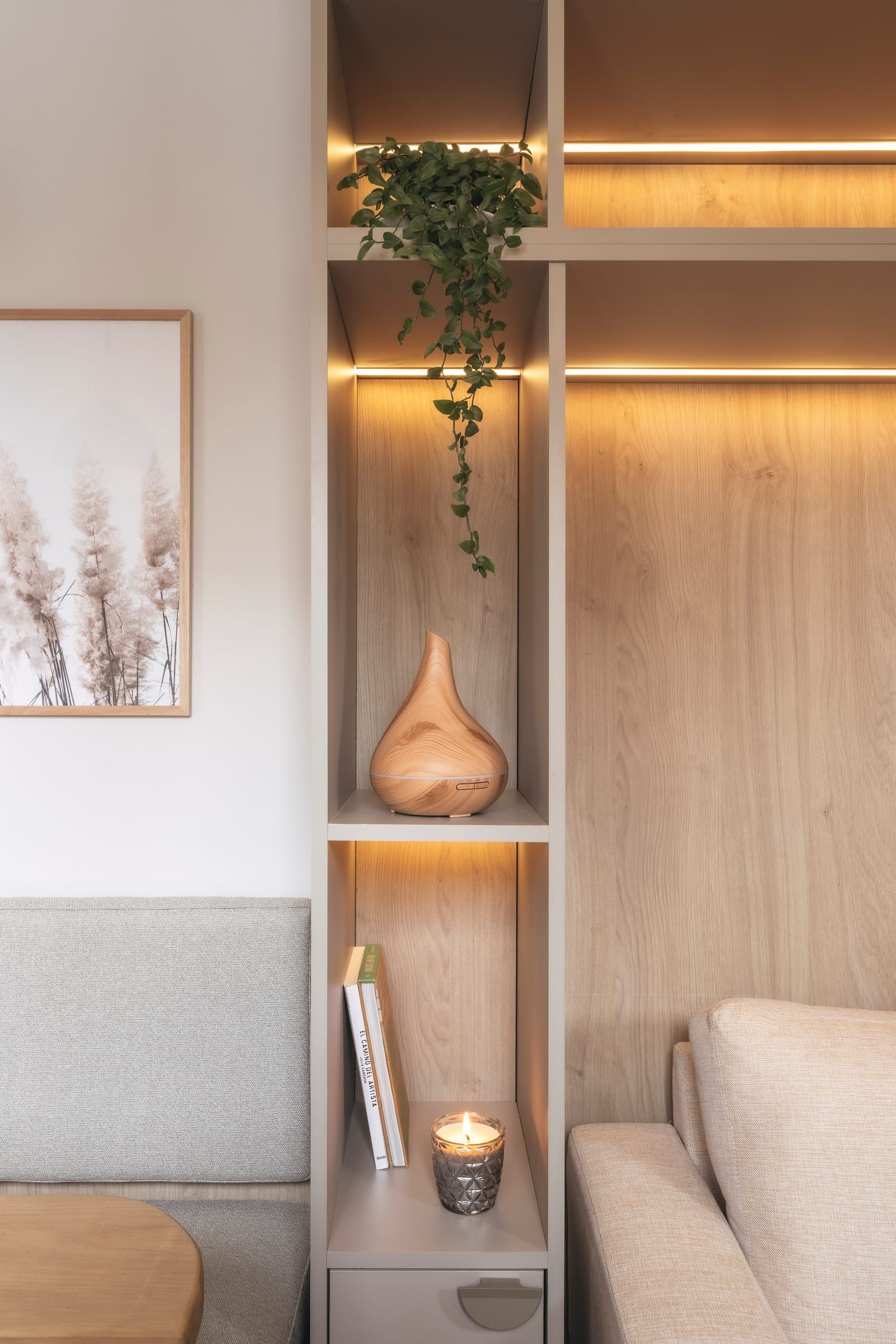 Nicho de madera con un cuadro, un difusor y libros bajo luz cálida