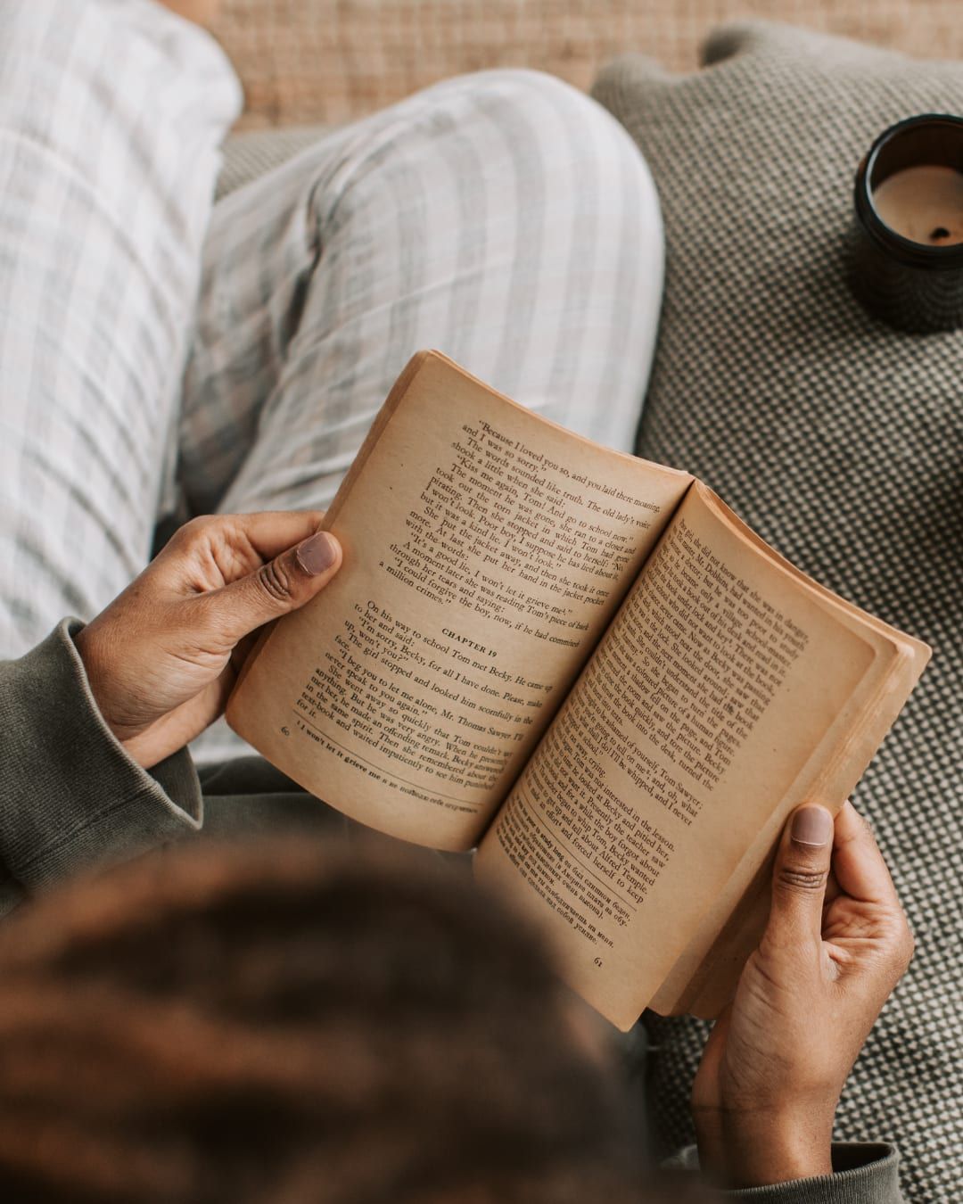 Mujer leyendo un libro, con una taza y sus anteojos al lado