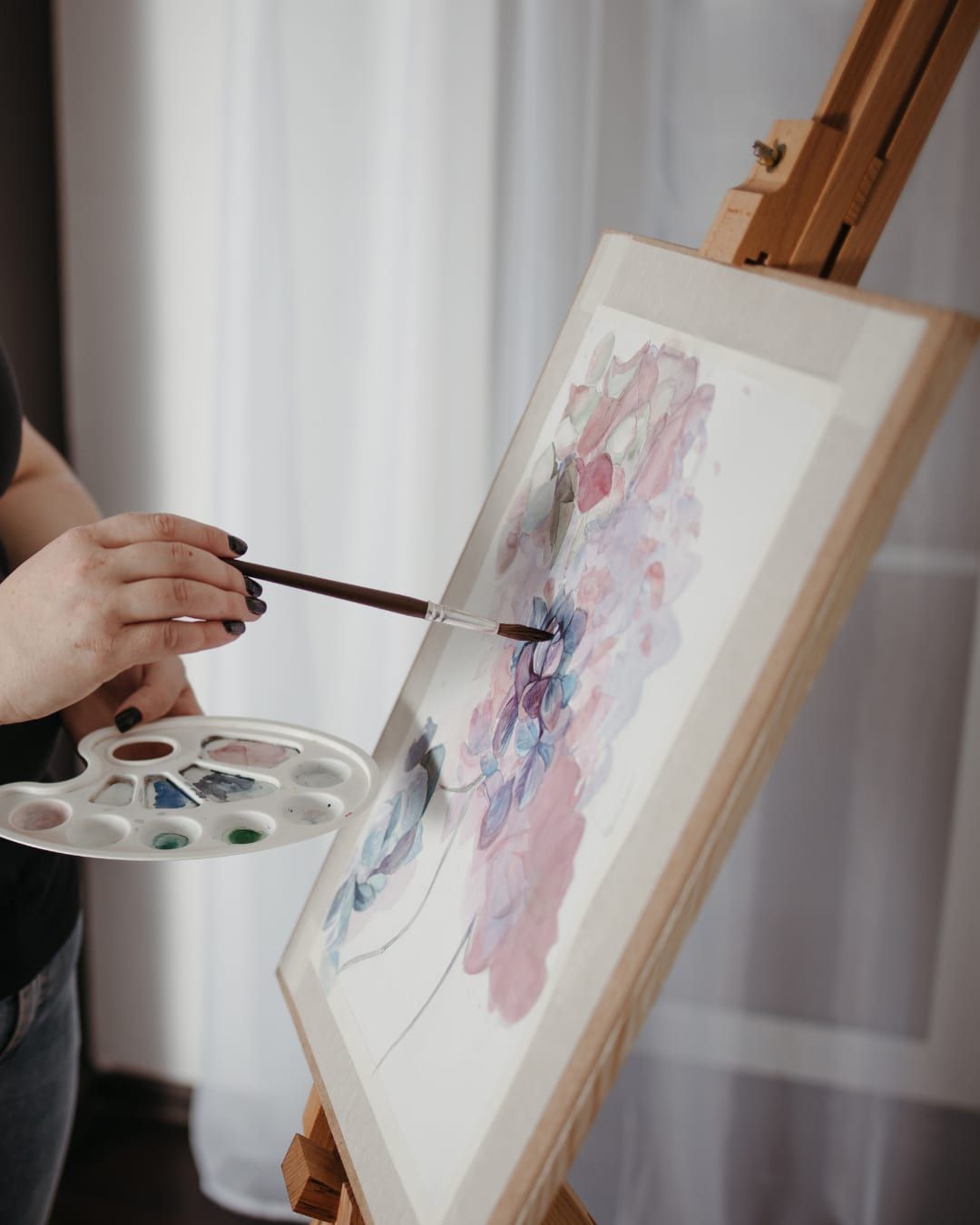 Persona pintando un cuadro en un atril, con la paleta en la mano
